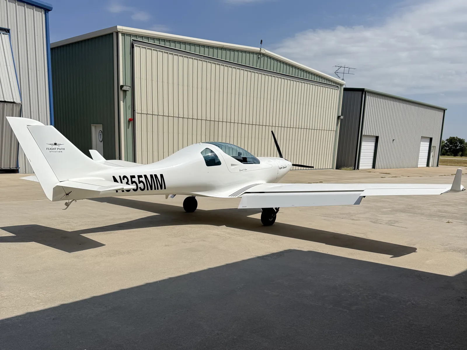 N355MM, a white Aerospool Dynamic WT-9, parked on the ramp in front of hangars