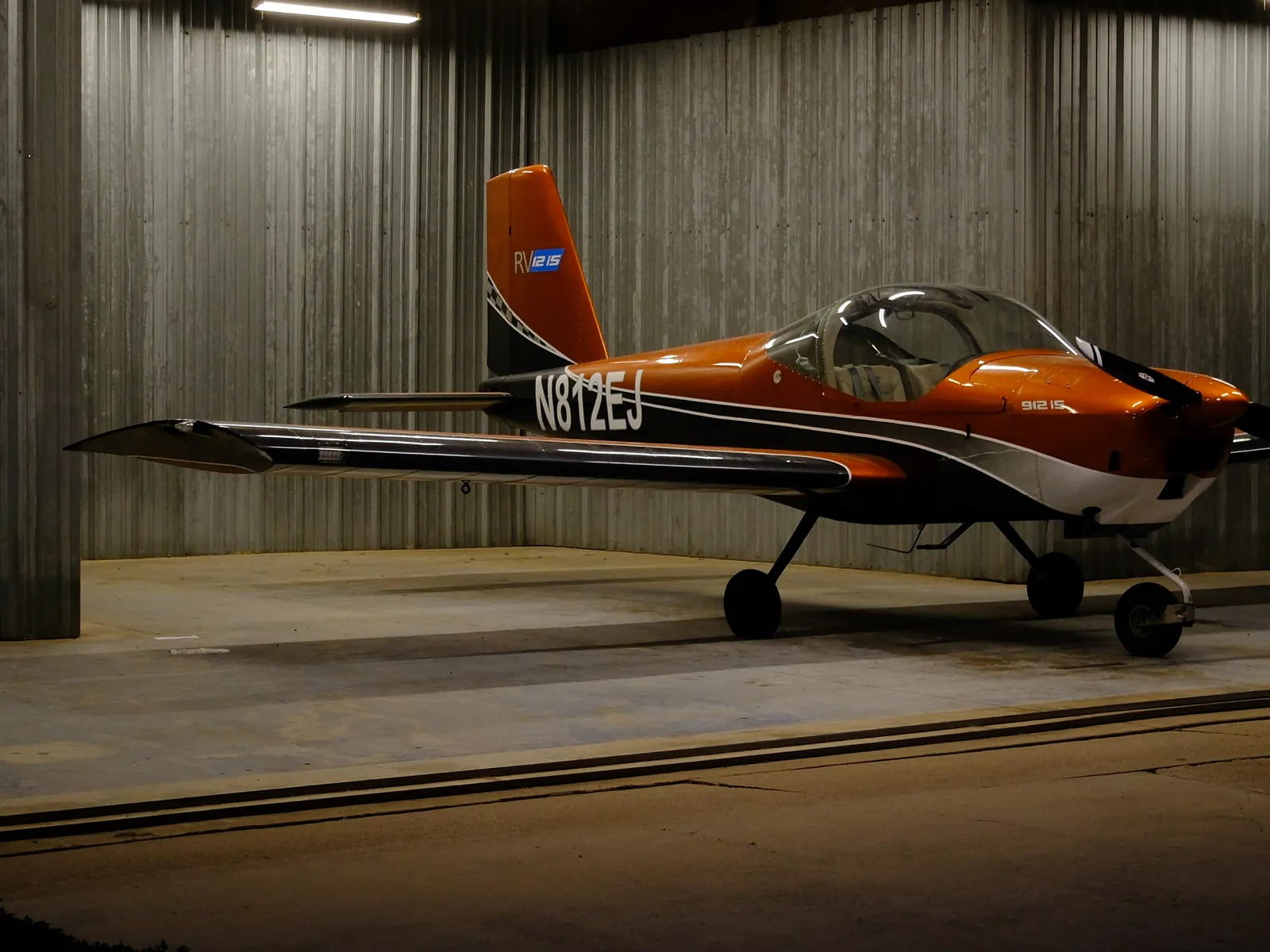 N812EJ, an orange Van's RV-12iS, parked in a lit hangar at dusk