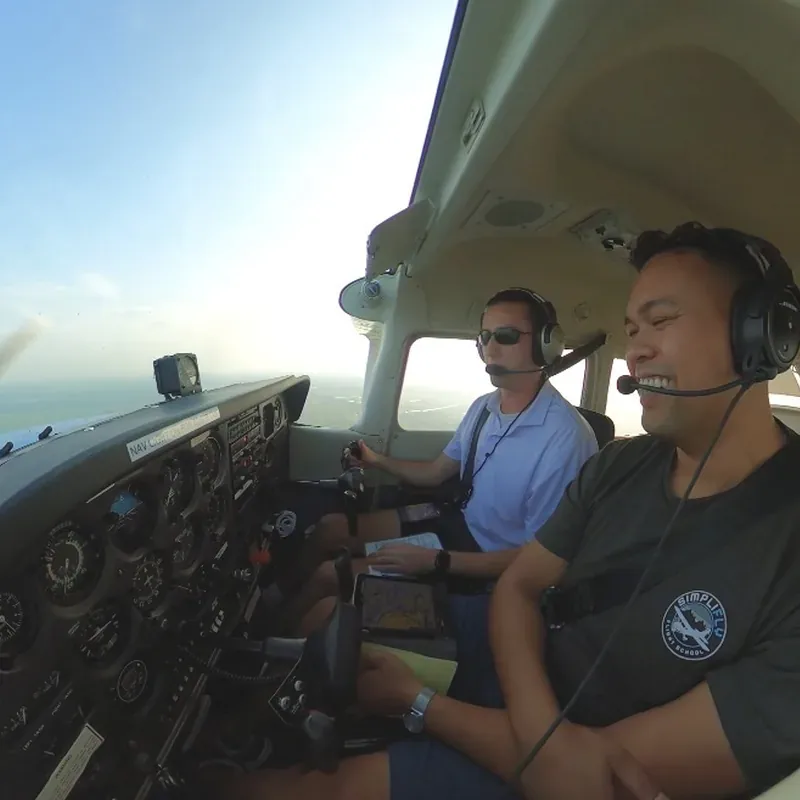 Instructor and student side by side in the cockpit, headsets on, in flight